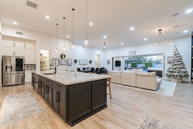 kitchen featuring visible vents, hanging light fixtures, appliances with stainless steel finishes, open floor plan, and light stone countertops