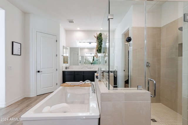 bathroom featuring wood finished floors, a sink, visible vents, double vanity, and a stall shower