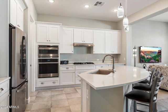 kitchen with stainless steel appliances, sink, white cabinetry, hanging light fixtures, and an island with sink