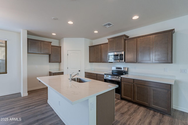 kitchen featuring a kitchen island with sink, dark wood-type flooring, sink, light stone countertops, and appliances with stainless steel finishes