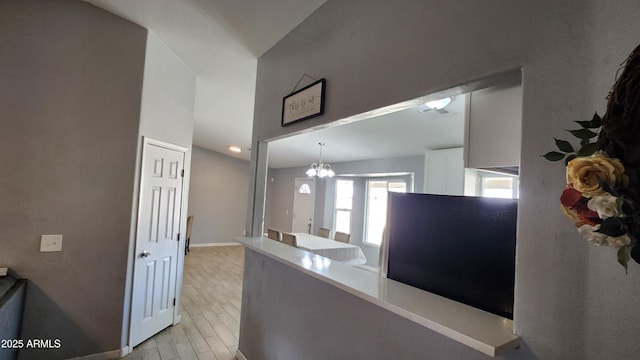 kitchen featuring light wood finished floors, white cabinetry, light countertops, baseboards, and a chandelier