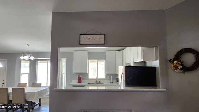 kitchen featuring a sink, white cabinetry, freestanding refrigerator, light countertops, and a chandelier