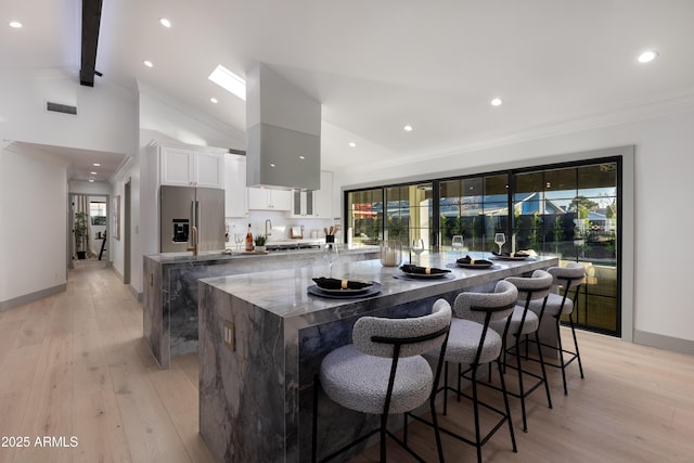 kitchen with white cabinets, lofted ceiling with beams, stainless steel fridge, light wood-type flooring, and a kitchen bar