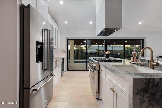 kitchen featuring sink, wall chimney range hood, high quality appliances, white cabinets, and light hardwood / wood-style floors