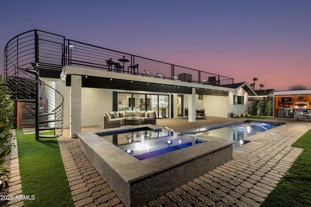 back house at dusk featuring a pool with hot tub, a balcony, an outdoor hangout area, and a patio