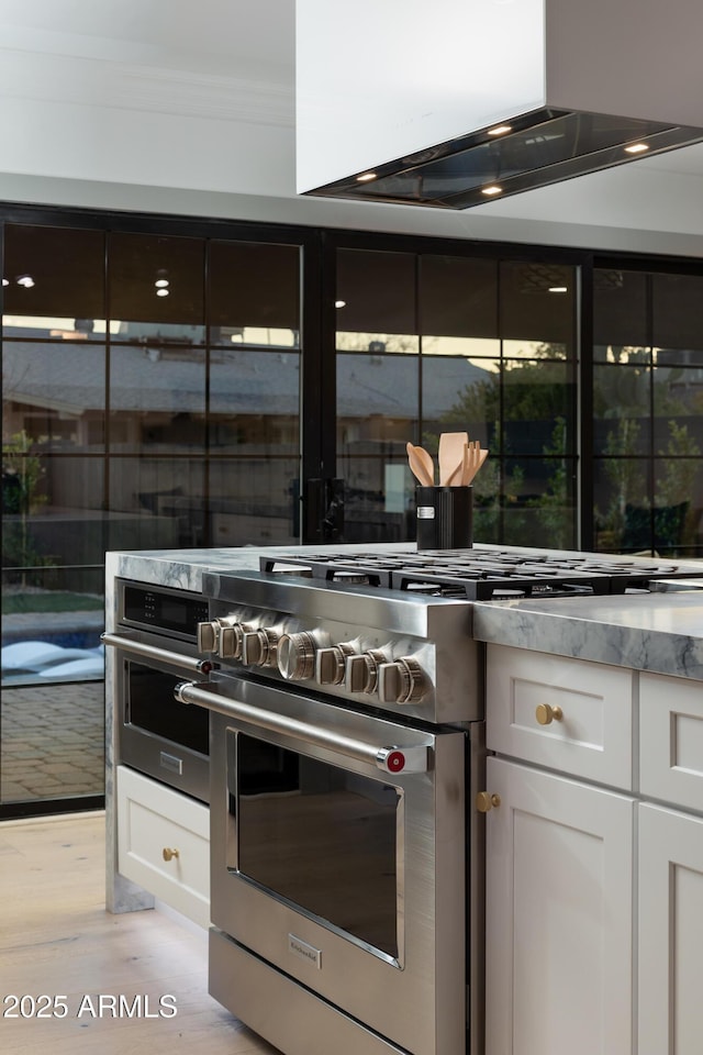 kitchen with white cabinets, light wood-type flooring, high end stove, ornamental molding, and island exhaust hood