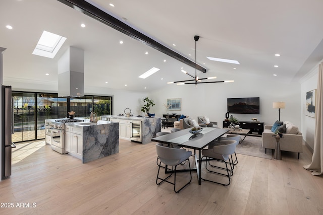 dining area with sink, vaulted ceiling with skylight, light wood-type flooring, beverage cooler, and a chandelier