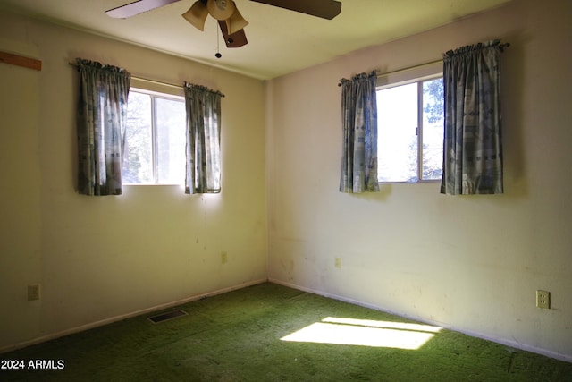 spare room featuring ceiling fan, dark colored carpet, and a wealth of natural light