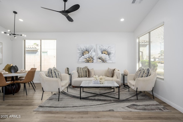 living room with vaulted ceiling, ceiling fan with notable chandelier, and light hardwood / wood-style flooring