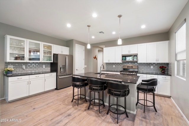 kitchen featuring appliances with stainless steel finishes, sink, decorative light fixtures, light hardwood / wood-style floors, and an island with sink