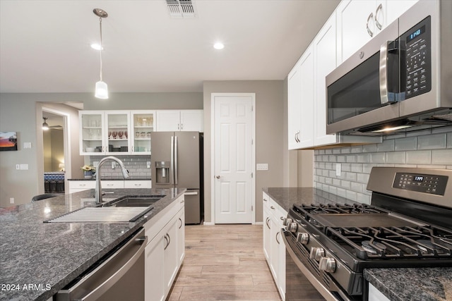 kitchen with appliances with stainless steel finishes, backsplash, light hardwood / wood-style flooring, white cabinets, and hanging light fixtures