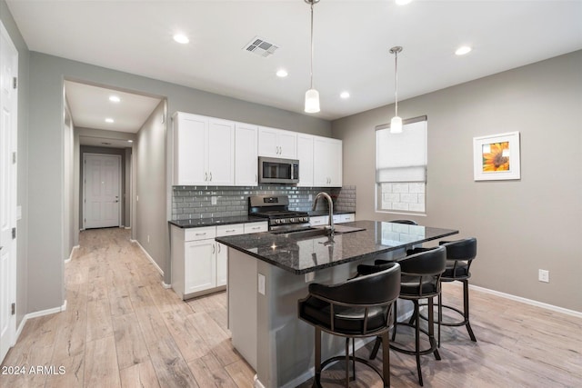 kitchen featuring white cabinetry, sink, stainless steel appliances, light hardwood / wood-style flooring, and a center island with sink