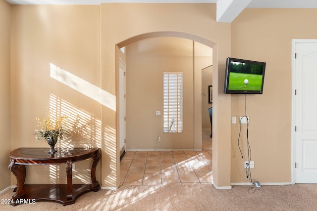 foyer featuring light carpet, light tile patterned floors, baseboards, and arched walkways