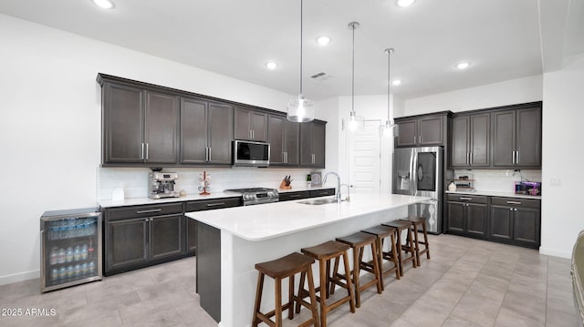 kitchen featuring a breakfast bar, appliances with stainless steel finishes, wine cooler, a center island with sink, and decorative light fixtures