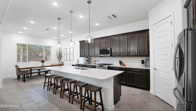 kitchen featuring appliances with stainless steel finishes, pendant lighting, backsplash, a kitchen breakfast bar, and a center island with sink