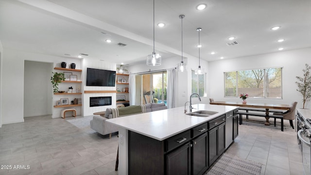 kitchen with pendant lighting, stainless steel stove, an island with sink, sink, and a kitchen bar