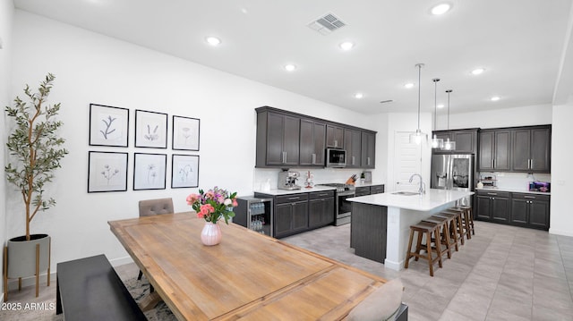 kitchen featuring a kitchen bar, sink, pendant lighting, stainless steel appliances, and a kitchen island with sink