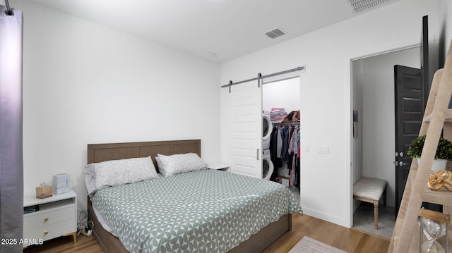 bedroom with stacked washer / drying machine, a spacious closet, a closet, hardwood / wood-style flooring, and a barn door