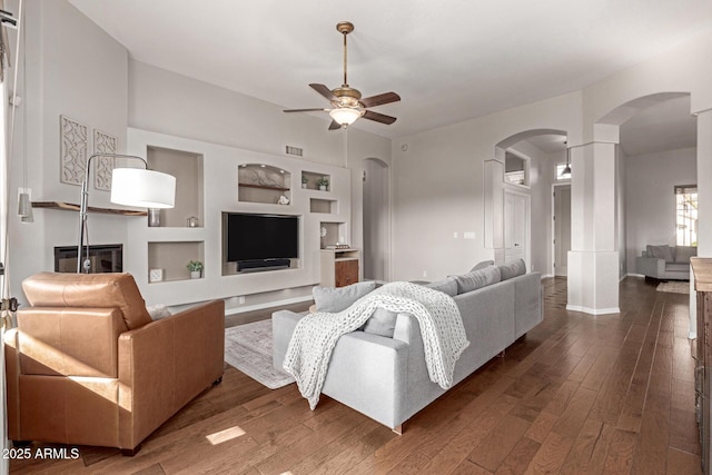 living room with built in shelves, ceiling fan, and dark hardwood / wood-style flooring