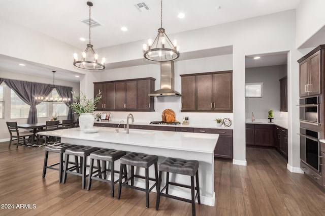 kitchen with pendant lighting, stainless steel gas stovetop, wall chimney exhaust hood, dark brown cabinetry, and a chandelier