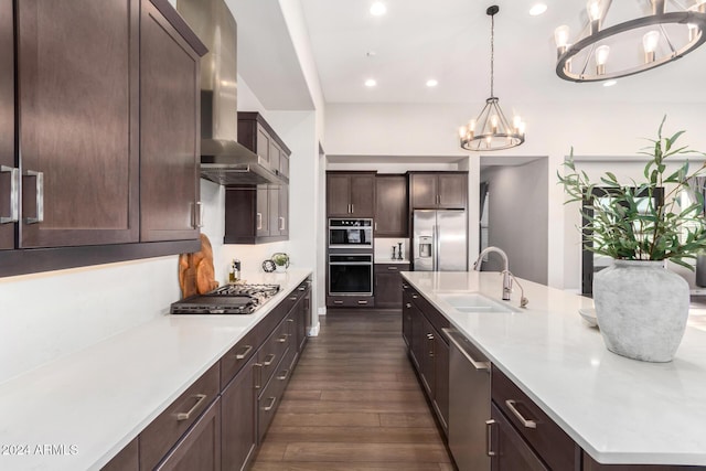 kitchen with an inviting chandelier, hanging light fixtures, sink, wall chimney exhaust hood, and appliances with stainless steel finishes