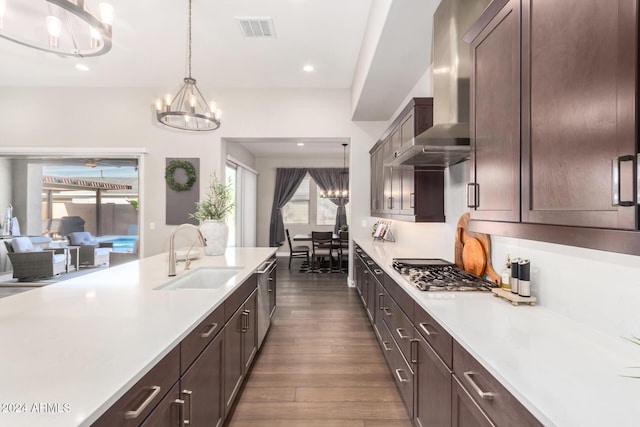 kitchen with appliances with stainless steel finishes, wall chimney range hood, sink, decorative light fixtures, and a chandelier