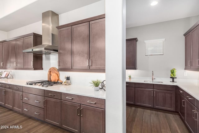 kitchen with sink, wall chimney exhaust hood, dark wood-type flooring, stainless steel gas stovetop, and dark brown cabinets