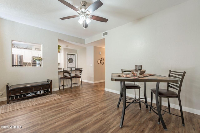 dining area with wood finished floors, baseboards, visible vents, ceiling fan, and stacked washer / drying machine