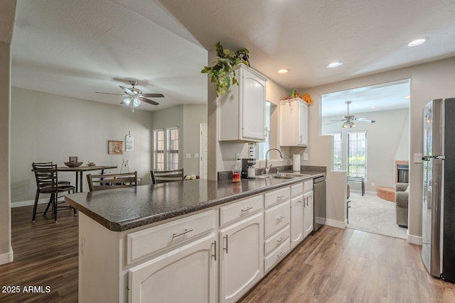 kitchen featuring a ceiling fan, a peninsula, a sink, stainless steel appliances, and dark wood-type flooring