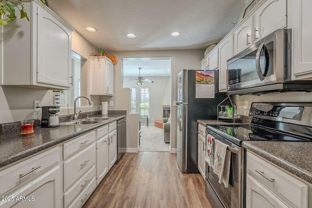 kitchen with dark countertops, ceiling fan, appliances with stainless steel finishes, white cabinets, and a sink