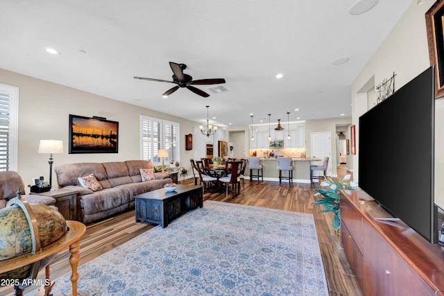 living room with ceiling fan with notable chandelier and light hardwood / wood-style floors