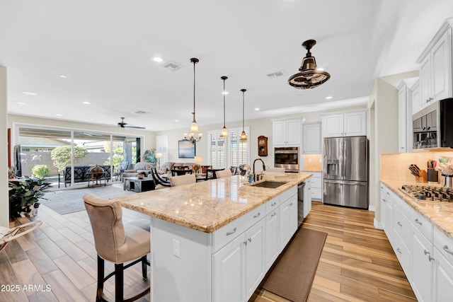 kitchen featuring sink, white cabinets, light stone counters, stainless steel appliances, and a center island with sink