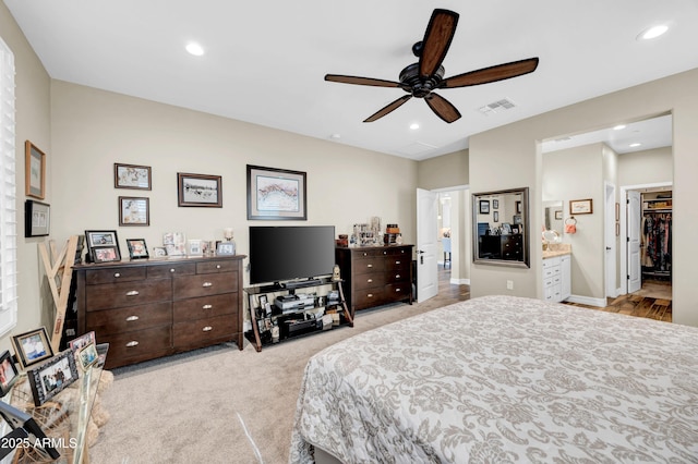 bedroom with light carpet, ensuite bath, a walk in closet, and ceiling fan