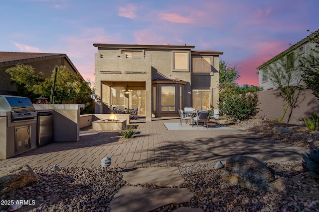 back house at dusk featuring area for grilling, a fire pit, and a patio area