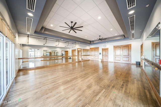 workout room with a tray ceiling, ceiling fan, and light wood-type flooring