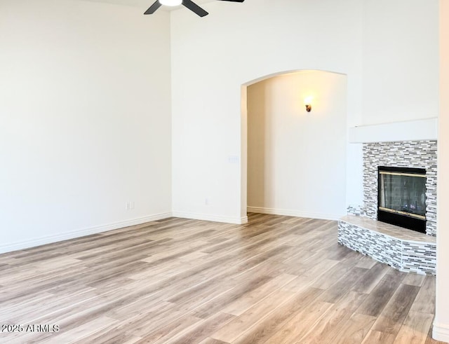 10722 W Quartz Dr, Casa Grande, AZ 85193 - unfurnished living room with a ceiling fan, light wood-style flooring, a tiled fireplace, a towering ceiling, and arched walkways