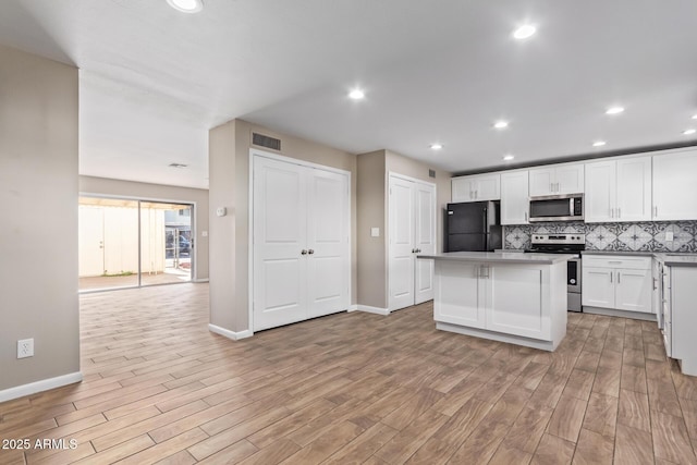 kitchen with light wood-type flooring, appliances with stainless steel finishes, white cabinetry, and a kitchen island