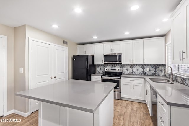 kitchen with appliances with stainless steel finishes, a center island, white cabinetry, tasteful backsplash, and sink