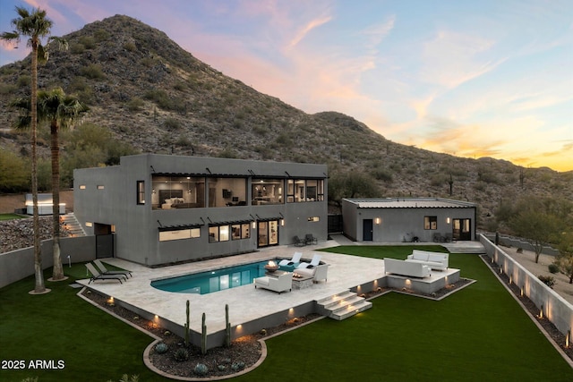 back house at dusk featuring a yard, a mountain view, an outdoor living space, a fenced in pool, and a patio