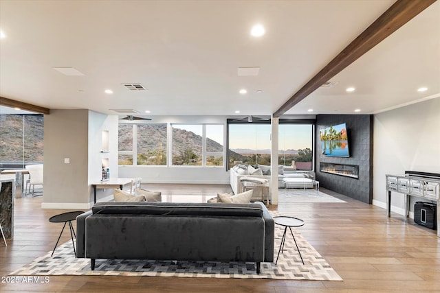 living room featuring a tile fireplace, beamed ceiling, and light wood-type flooring