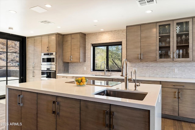 kitchen with an island with sink, dark hardwood / wood-style flooring, sink, and double oven