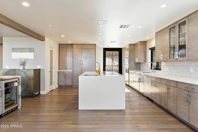 kitchen featuring wine cooler, sink, dark hardwood / wood-style floors, a kitchen island with sink, and decorative backsplash