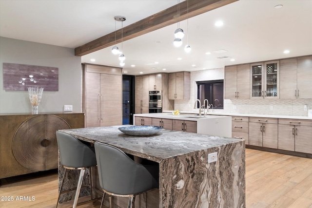 kitchen with pendant lighting, light wood-type flooring, backsplash, a large island, and beam ceiling