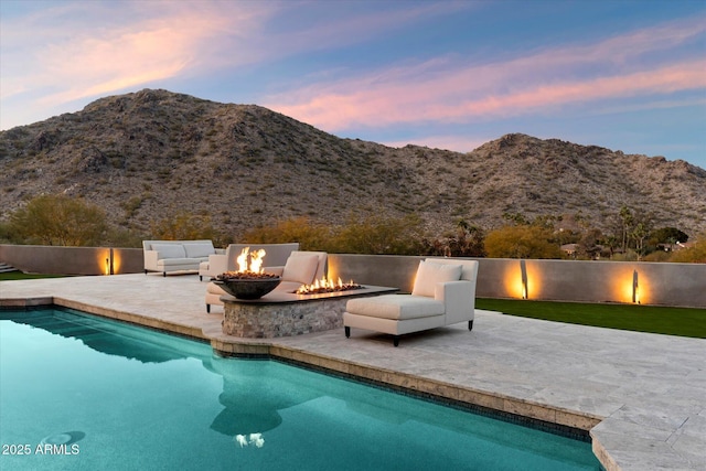 pool at dusk with a mountain view, a fire pit, and a patio area