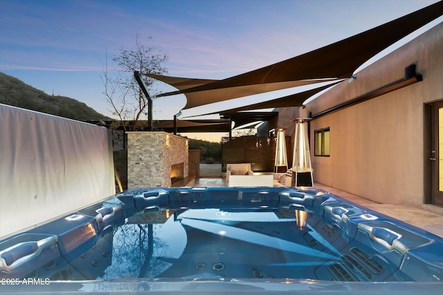 pool at dusk featuring an outdoor fireplace