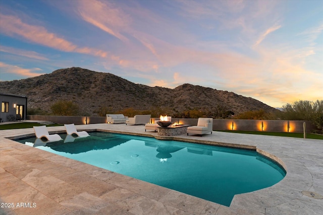 pool at dusk with a mountain view, a patio area, and a fire pit