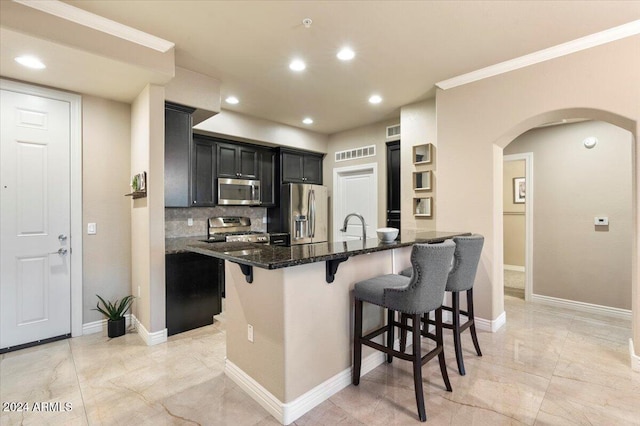 kitchen with backsplash, stainless steel appliances, dark stone countertops, crown molding, and a breakfast bar