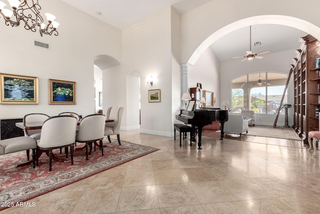 tiled dining room featuring ceiling fan with notable chandelier, a towering ceiling, visible vents, and baseboards