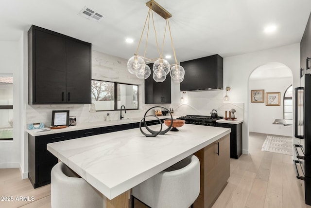 kitchen with dark cabinetry, visible vents, arched walkways, black appliances, and tasteful backsplash