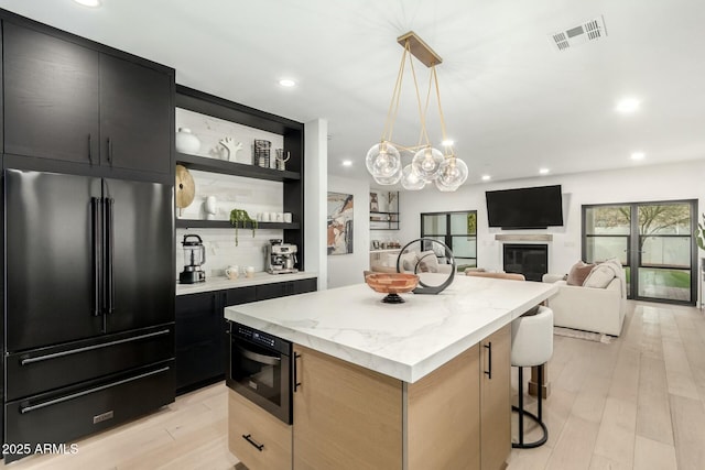 kitchen featuring dark cabinetry, visible vents, a kitchen island, open shelves, and high end black refrigerator